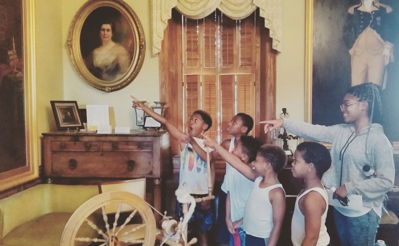 Tamysinae giving a tour at the museum to her family.   They are pointing at the museum's portrait of George Washington.